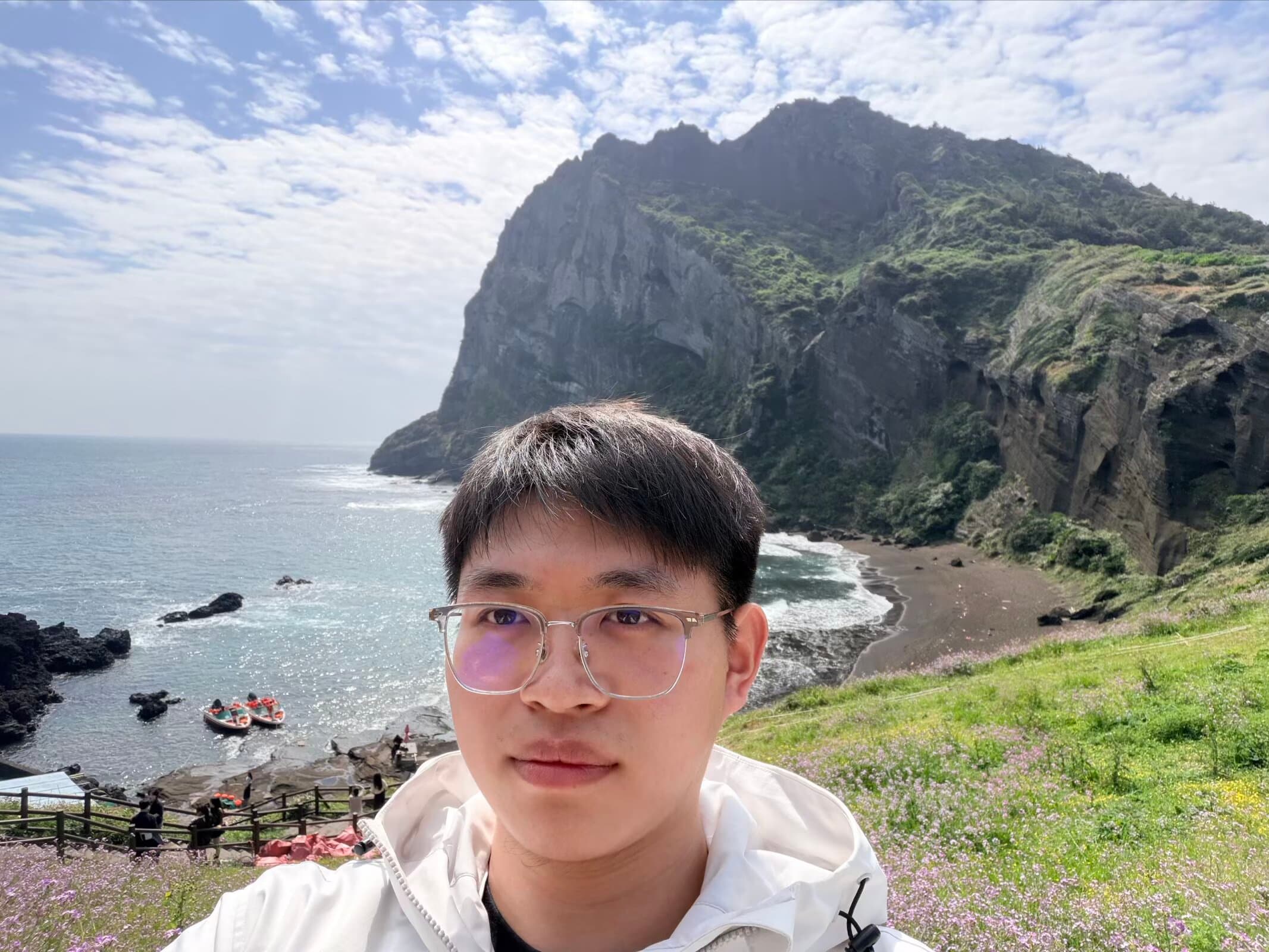 Lyu Junyan wearing glasses beside the sea and a coastal cliff.